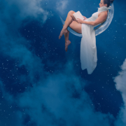 Femme en robe blanche flottant dans un ciel étoilé bleu profond, entourée de nuages, dans une ambiance onirique et spirituelle.